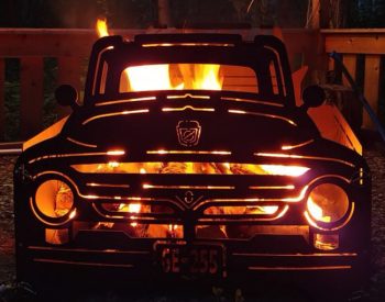 Plasma-cut steel fire pit in the shape of a classic pickup truck glowing with fire at night.