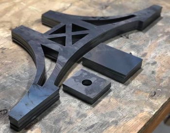 Stack of plasma-cut steel bracket components arranged on a worn wooden workbench.
